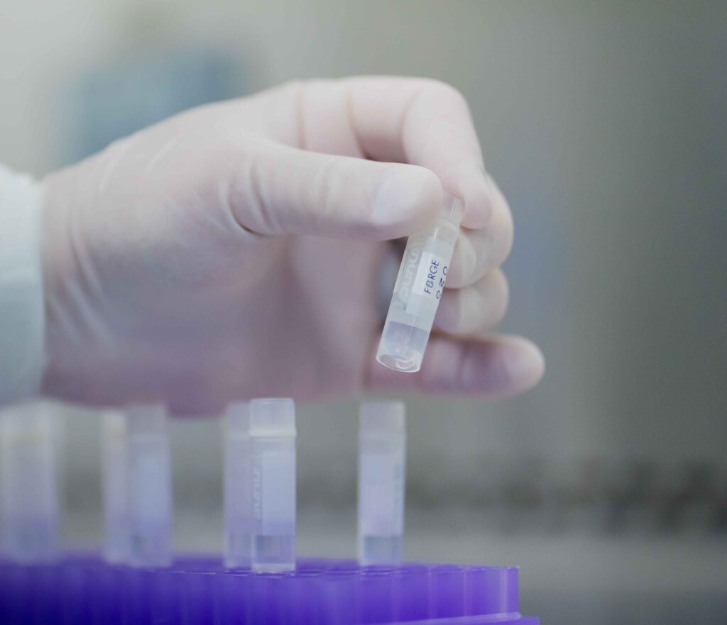 The gloved hand of a technician holding a vial of drug substance.