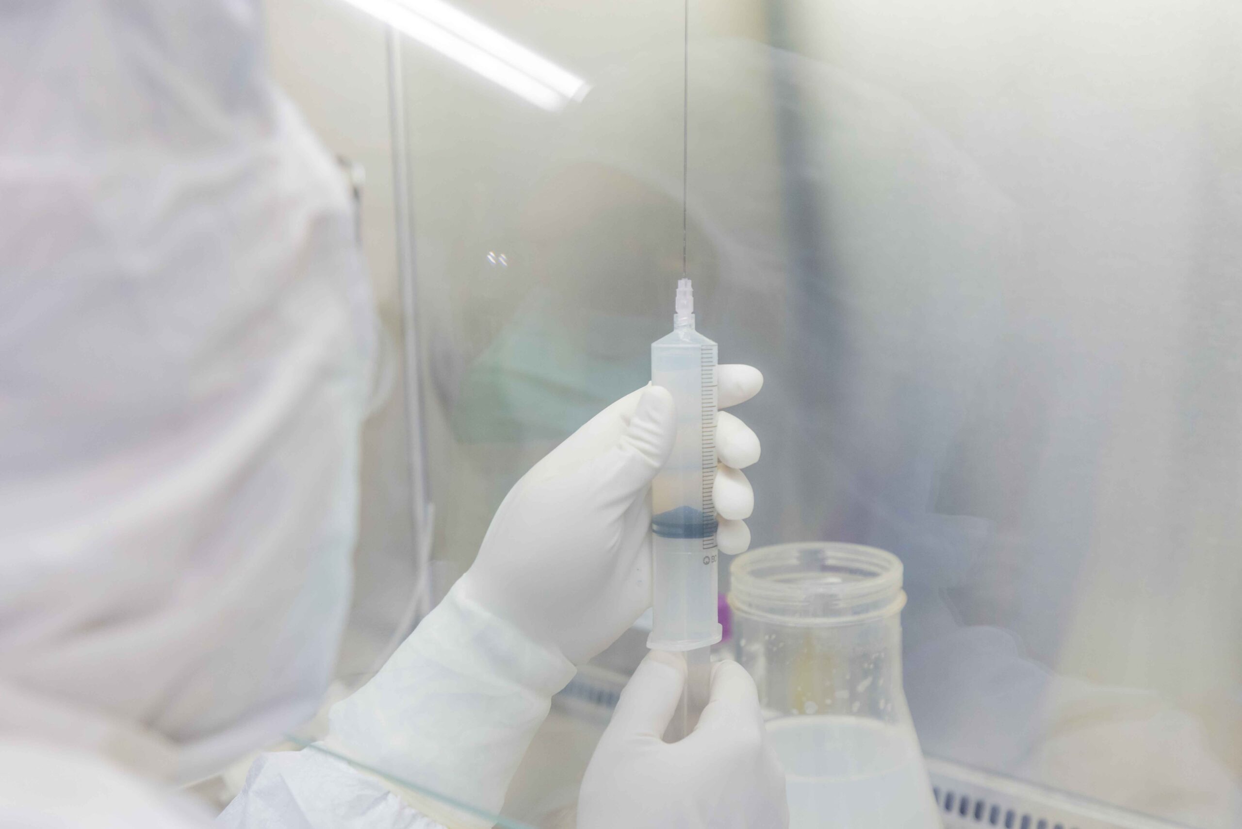 Partial view of a technician in full PPE holding drug substance in one of Forge's cGMP suites.