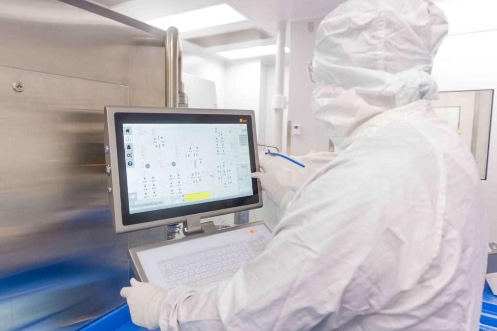 A scientist in full PPE programming a run in a cGMP suite.